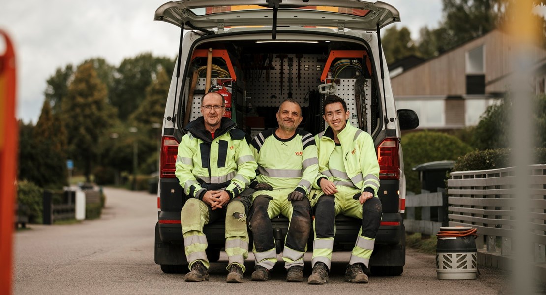 Tre montörer sitter vid en servicebil och tittar in i kameran